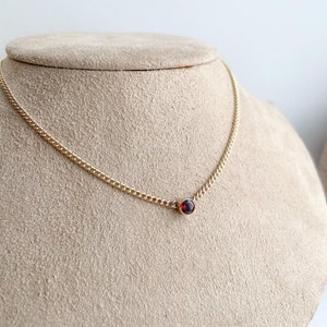May include: A delicate gold chain necklace with a single red gemstone pendant.