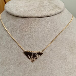 May include: A gold necklace with a triangular pendant featuring a delicate floral design.