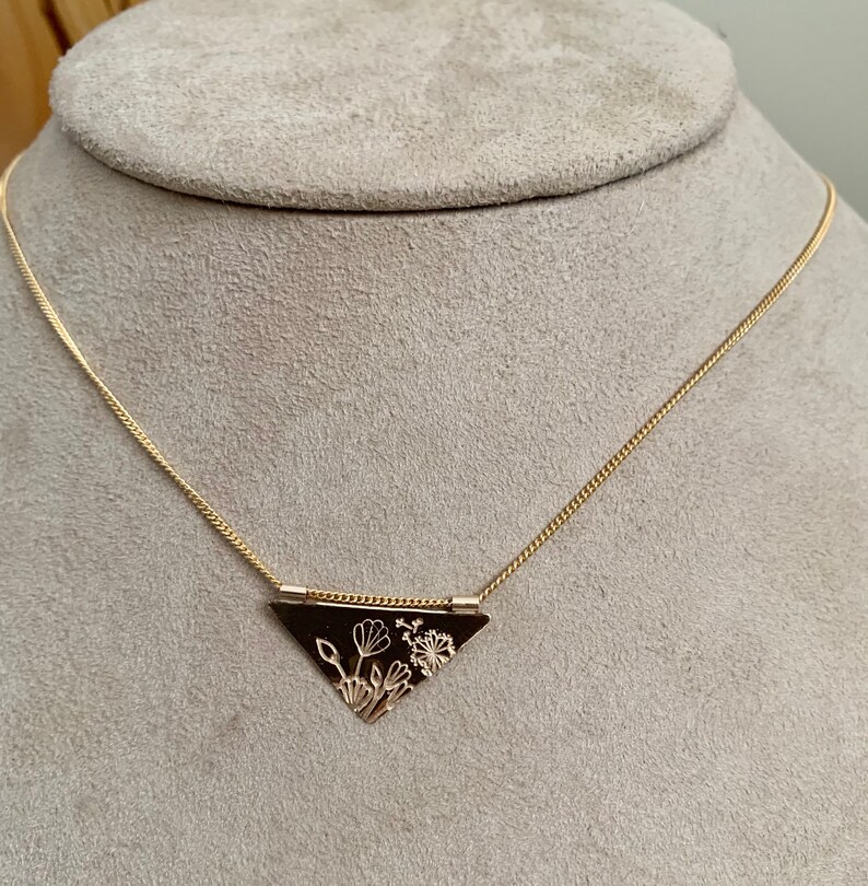 May include: A gold necklace with a triangular pendant featuring a delicate floral design.