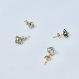 May include: Three pairs of gold earrings with clear and grey rough cut gemstones. The earrings have a gold post and back.