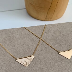 May include: Two gold necklaces with triangular pendants. One pendant is plain, while the other has a floral design.