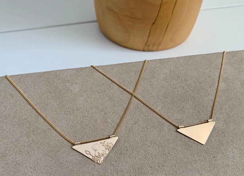 May include: Two gold necklaces with triangular pendants. One pendant is plain, while the other has a floral design.