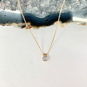 May include: A delicate gold chain necklace with a small, round, iridescent gemstone pendant.