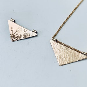 May include: Two gold triangle pendants, one with a floral design and the other with a hammered texture, on a gold chain.