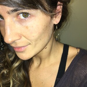 May include: A woman wearing a black top with gold dangle earrings featuring a black teardrop-shaped stone.