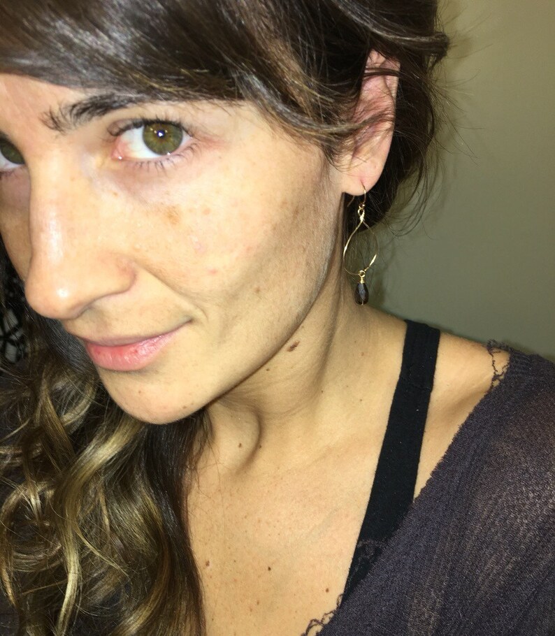 May include: A woman wearing a black top with gold dangle earrings featuring a black teardrop-shaped stone.
