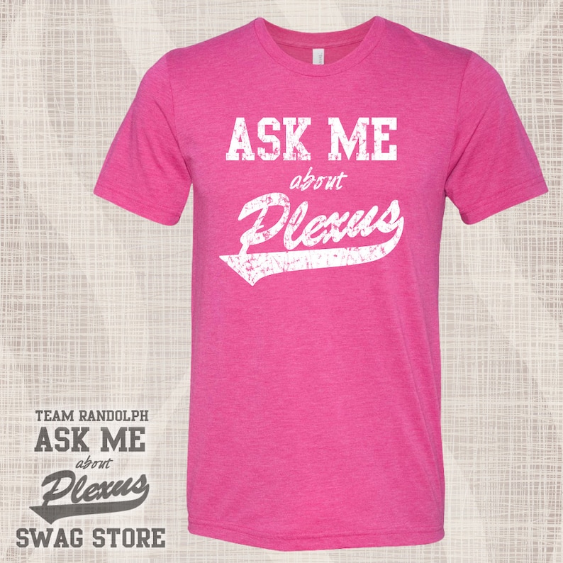 May include: Pink t-shirt with white text that reads "Ask Me about Plexus". The text is in a vintage style font with a distressed look. The shirt is a heather pink color and has a crew neck.