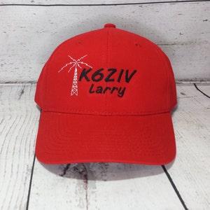 May include: A bright red baseball cap featuring an embroidered white palm tree graphic next to the black text K6ZIV and the name Larry embroidered in black script below the call sign on the front panel of the hat.