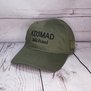 May include: A green baseball cap with black embroidered text that reads "KD3MAD Michael" and a small American flag patch on the side.