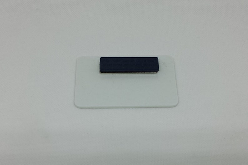 Peut inclure: Une &eacute;tiquette de nom rectangulaire blanche avec une bande magn&eacute;tique bleu fonc&eacute;.