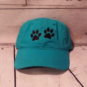 May include: A turquoise blue baseball cap with black paw prints embroidered on the front.
