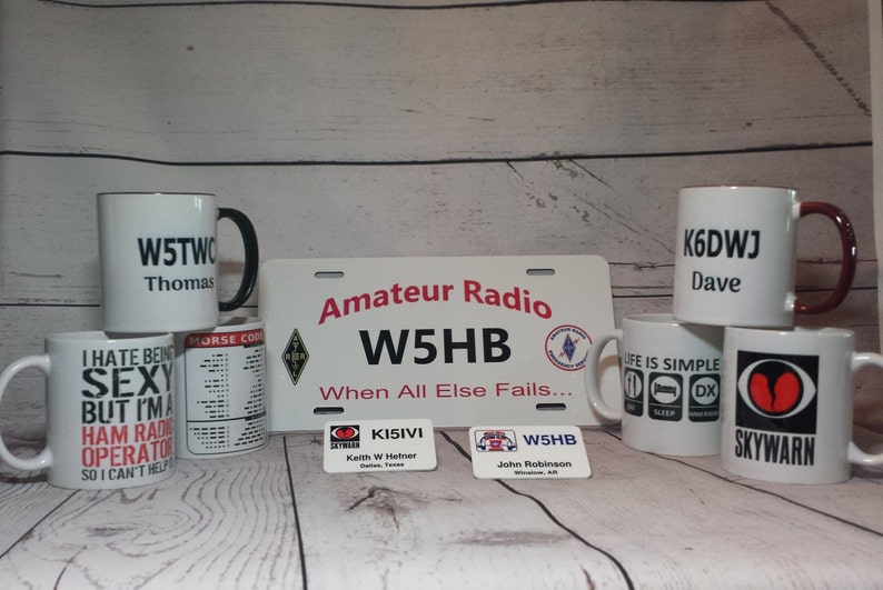 Peut inclure: Une collection de tasses en c&eacute;ramique blanche avec diff&eacute;rents motifs et textes. Les tasses pr&eacute;sentent des indicatifs d'appel, du code Morse et la phrase "Amateur Radio W5HB When All Else Fails..." Les tasses sont dispos&eacute;es sur une surface en bois avec deux petites &eacute;tiquettes rectangulaires.
