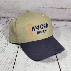 May include: A tan baseball cap with a dark blue brim. The front features an embroidered orange palm tree graphic next to the dark blue text N4CGR and the name Mike embroidered in dark blue thread below the alphanumeric characters.