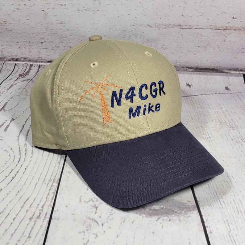 May include: A tan baseball cap with a dark blue brim. The front features an embroidered orange palm tree graphic next to the dark blue text N4CGR and the name Mike embroidered in dark blue thread below the alphanumeric characters.