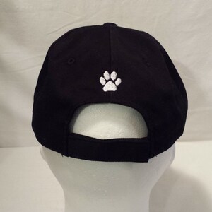 May include: Black baseball cap with a white paw print embroidered on the back.