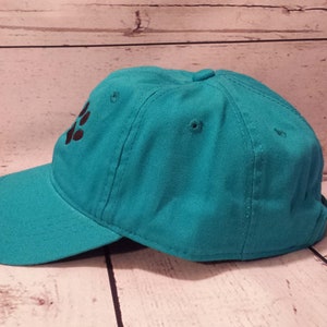 May include: A teal blue baseball cap with a black paw print design.
