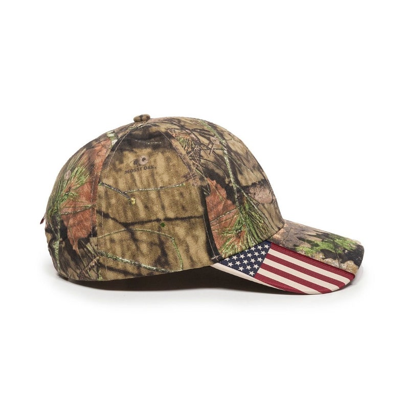 May include: A camouflage baseball cap with a red, white, and blue American flag on the brim. The cap has the words "MOssy OAK" printed on the back.