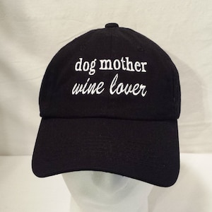 May include: Black baseball cap with white embroidered text that reads "dog mother wine lover".