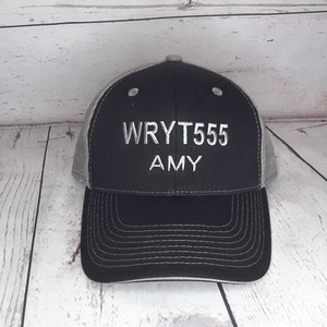 May include: A black and gray trucker hat with the text "WRYT555 AMY" embroidered in white on the front.