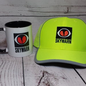 May include: A white mug with a black handle and a black and red logo that says "SKYWARN" on it. Next to the mug is a yellow and gray mesh baseball cap with the same logo on the front.