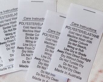 Könnte beinhalten: Sechs weiße Pflegehinweisetiketten mit schwarzem Text. Die Etiketten sind für Polyester/Elasthan-Gewebe und enthalten Anweisungen zum Waschen, Trocknen und Bügeln. Die Etiketten werden in Australien hergestellt. Im Hintergrund befindet sich ein Schwarzweißbild einer Nähmaschine mit dem Text "RUBYJAM FABRIC".