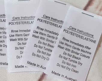 Könnte beinhalten: Sechs weiße Pflegeetiketten mit schwarzem Text, der die Pflegehinweise für Polyester- und Elastan-Gewebe beschreibt. Die Etiketten lauten "Pflegehinweise Polyester/Elastan" und enthalten Anweisungen zum sofortigen Ausspülen nach dem Waschen, zum Waschen mit ähnlichen Farben in der Maschine bei niedriger Temperatur, zum Verzicht auf Bleichen, zum Verzicht auf Trockner, zum Verzicht auf Bügeln und zum Verzicht auf chemische Reinigung. Die Etiketten tragen außerdem den Hinweis "Hergestellt in Australien". Unter den Etiketten befindet sich ein Schwarzweißbild einer Nähmaschine mit einem Herzen und dem Text "RUBYJAM FABRIC".