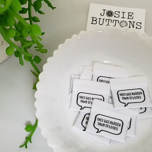 Puede incluir: Un tazón blanco lleno de etiquetas de tela blanca con texto negro que dice "This was harder than it looks" en un globo de diálogo. Las etiquetas son para proyectos de costura.