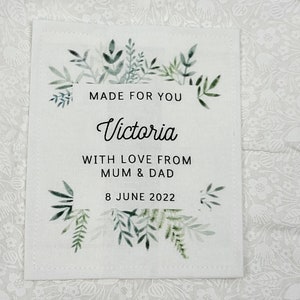 May include: A white fabric tag with a green leafy border. The tag says "Made for you Victoria with love from Mum & Dad 8 June 2022".
