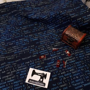 K&ouml;nnte beinhalten: Ein dunkelblauer Stoff mit wei&szlig;em Text darauf gedruckt. Der Text ist Code aus einem Computerprogramm. Der Stoff hat ein N&auml;hmaschinenlogo mit dem Text "Rubyjam Fabric" darauf gedruckt.