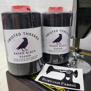 May include: Two spools of black overlocker thread, each labeled "Twisted Threads Raven Black 5000m 100% Spun Polyester Overlocker Thread". The spools are sitting on a black sewing machine with a white sticker that says "Rubyjam Fabric" on it.