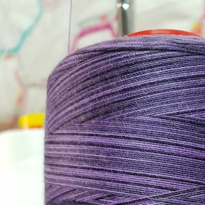 May include: A spool of purple and black thread wound around a white bobbin.