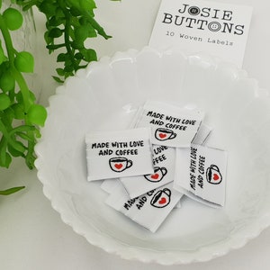 Puede incluir: Diez etiquetas tejidas blancas con el texto "Made with Love and Coffee" y un pequeño corazón rojo en un gráfico de taza de café. Las etiquetas están en un tazón blanco.