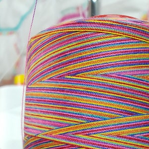 May include: Close-up of a multi-coloured thread spool. The thread is tightly wound, showing a vibrant mix of pink, yellow, blue, and orange. This thread is likely for sewing, embroidery, or other textile crafts.