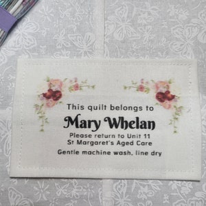 May include: A white fabric label with floral accents and black text that reads "This quilt belongs to Mary Whelan. Please return to Unit 11 St Margaret's Aged Care. Gentle machine wash, line dry."