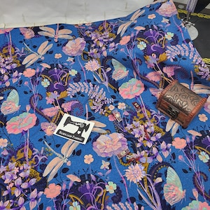 Puede incluir: Tela azul con un patrón floral que presenta libélulas, mariposas y diseños de cachemira. La tela tiene un brillo sutil y es perfecta para proyectos de manualidades.