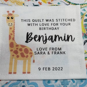May include: A white fabric label with a giraffe illustration, the text "THIS QUILT WAS STITCHED WITH LOVE FOR YOUR BIRTHDAY Benjamin LOVE FROM SARA & FRANK 9 FEB 2022", and a stitched border.