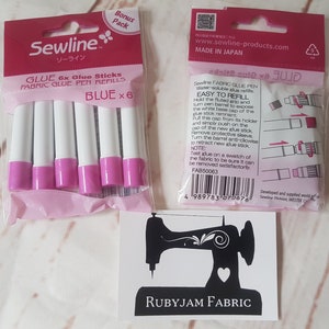 May include: A package of six blue fabric glue pen refills from Sewline. The package is pink and white with the brand name and product description printed on it. The glue sticks are white with pink caps. The package also includes instructions on how to refill the glue pen.