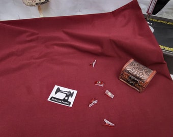 May include: A burgundy fabric swatch with a small white label that says "Ruby Jam Fabric" and a sewing machine icon. There are also several clear plastic clips scattered on the fabric and a small wooden box with an ornate design.