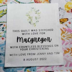 Puede incluir: Una etiqueta de tela blanca con texto negro que dice "This quilt was stitched with love for MacGregor with countless blessings on your christening with love from Jenny and Tim 8 August 2022".