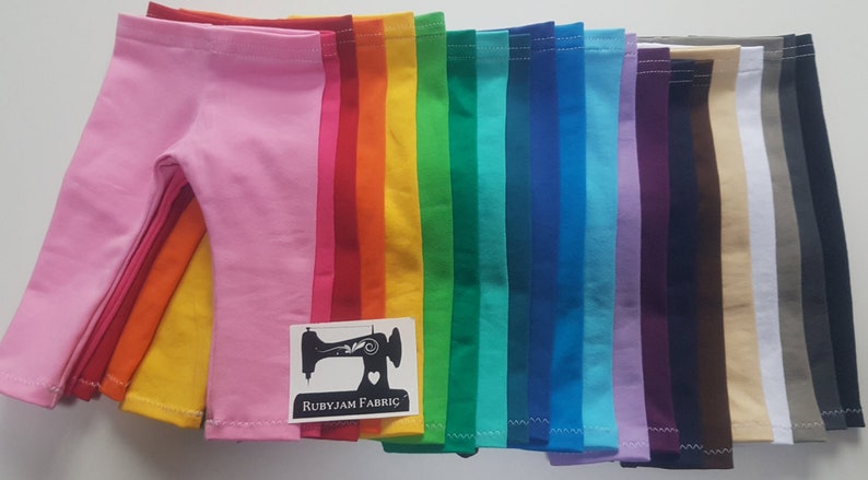 May include: A stack of 17 pairs of colorful leggings for dolls. The leggings are in a rainbow of colors, including pink, red, orange, yellow, green, blue, purple, brown, beige, and gray. The leggings are all folded in half and stacked on top of each other. The leggings are made of a soft, stretchy fabric. The leggings are perfect for adding a pop of color to any doll's outfit.  Rubyjam Fabric.