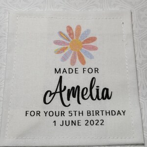 May include: White fabric label with a colourful flower design. The text reads "Made for Amelia for your 5th birthday 1 June 2022".