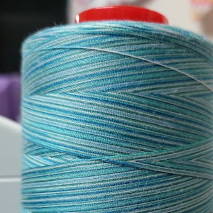 May include: A spool of teal, blue, and white striped thread. The thread is wound tightly around the spool.
