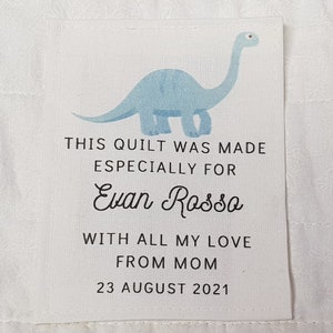 May include: A blue dinosaur illustration on a white tag with the text "This quilt was made especially for Evan Rosso with all my love from Mom 23 August 2021".