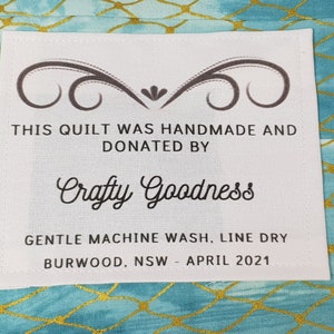 May include: White fabric label with black text stating "This quilt was handmade and donated by Crafty Goodness. Gentle machine wash, line dry. Burwood, NSW - April 2021."