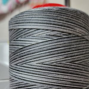 May include: A spool of grey and white thread wound tightly together. The thread is smooth and shiny, and the spool is made of a sturdy material.