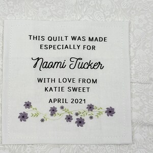 May include: A white square label with black text that reads "THIS QUILT WAS MADE ESPECIALLY FOR Naomi Tucker WITH LOVE FROM KATIE SWEET APRIL 2021." The label has a floral design.