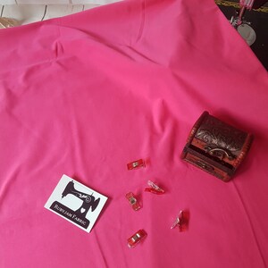 May include: A bright pink fabric swatch with a small white label that says "RubyJam Fabric" and a sewing machine icon. There are also several red plastic clips scattered on the fabric.