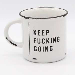 Puede incluir: Taza de cerámica blanca con borde negro y texto negro que dice "KEEP FUCKING GOING".