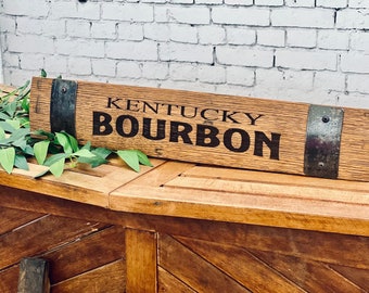 Op de afbeelding: Een houten bord met metalen accenten met de tekst "Kentucky Bourbon". Het bord is gemaakt van gerecycled hout en heeft een rustieke uitstraling.
