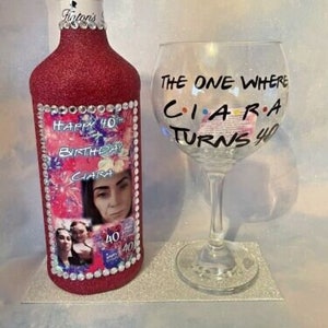 Op de afbeelding: Roze glitterfles met een foto van een vrouw en de tekst "Happy 40th Birthday Ciara". Naast de fles staat een helder glas met de tekst "The One Where Ciara Turns 40".